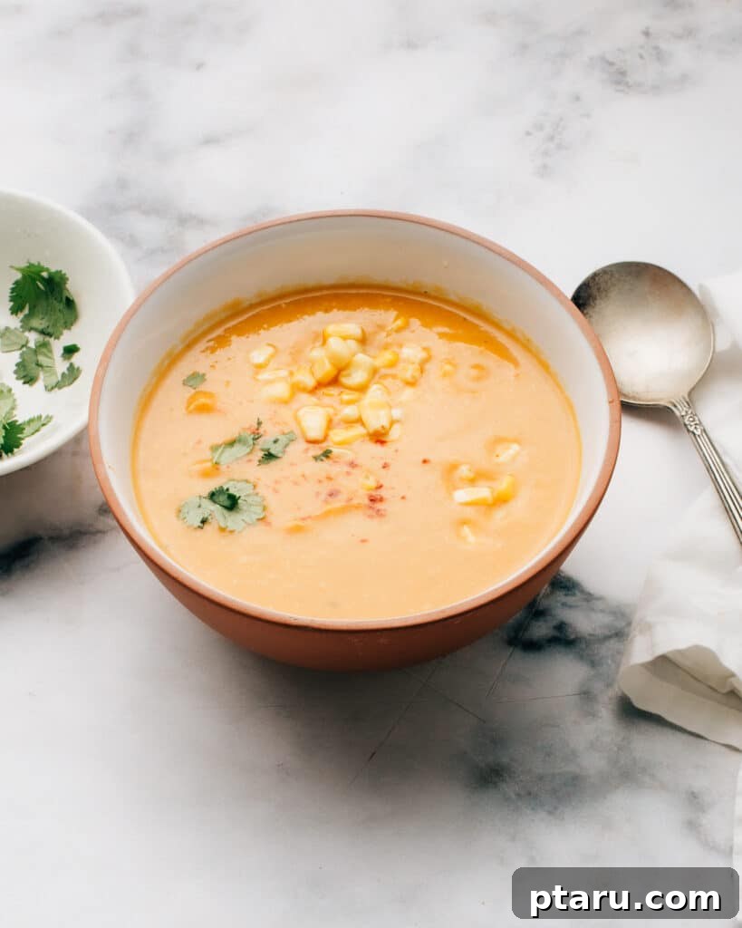 Tropical Sweet Potato and Corn Chowder 2 A beautifully presented bowl of vibrant sweet potato, coconut, and corn soup, garnished with fresh green cilantro leaves, ready to be enjoyed.