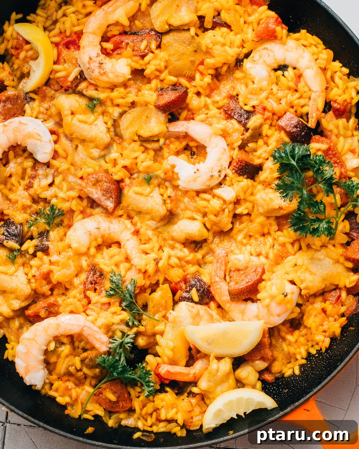 Spanish Surf and Turf Paella 2 A vibrant, colorful Chorizo Paella with shrimp and chicken in a large pan, garnished with fresh parsley and lemon wedges.