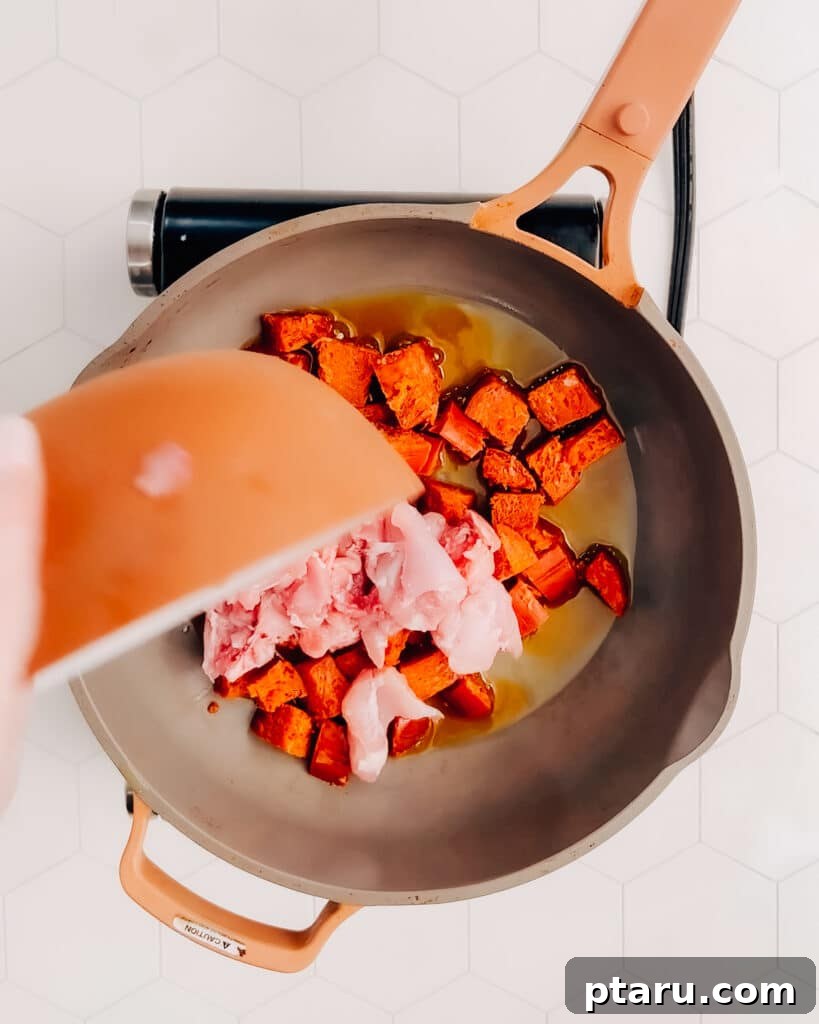 Spanish Surf and Turf Paella 3 Adding diced chicken and sliced cured chorizo to hot olive oil in a large frying pan, browning them for the paella base.