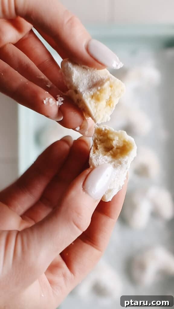 Kourabiedes Traditional Greek Christmas Butter Cookies 12 A freshly baked Kourabiedes cookie, gently broken in half to reveal its tender, crumbly interior and rich almond texture, signifying its melt-in-your-mouth quality and readiness to be savored.