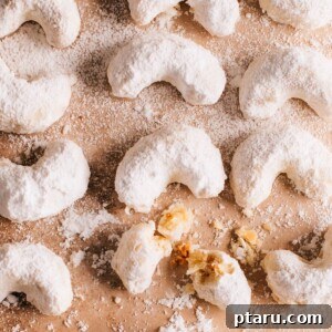 A batch of Kourabiedes or Greek Christmas Cookies on a surface with one cookie broken.
