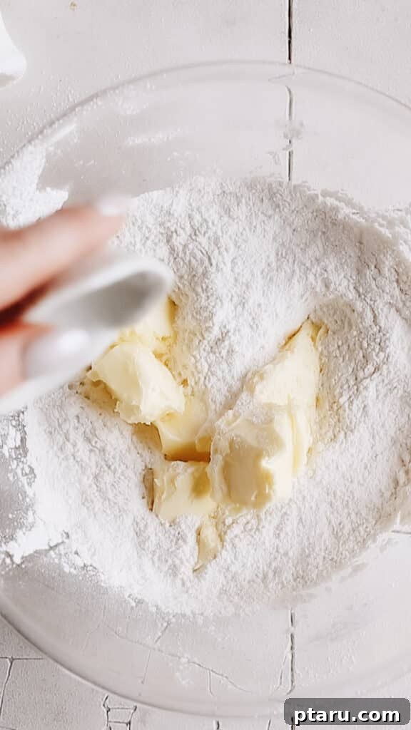 Kourabiedes Traditional Greek Christmas Butter Cookies 4 Softened butter being carefully added to a bowl of flour mixture, showcasing the initial step of the reverse creaming method for Kourabiedes dough, which results in a tender crumb.
