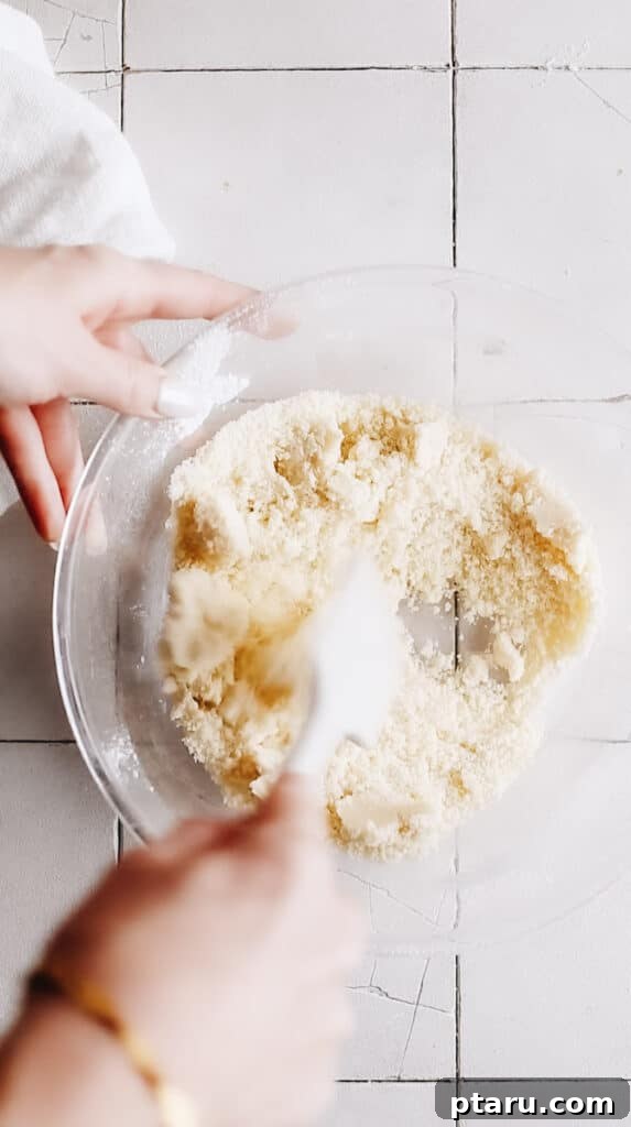 Kourabiedes Traditional Greek Christmas Butter Cookies 6 A spatula gently mixing the Kourabiedes dough in a bowl, demonstrating the cohesive texture forming after the ingredients are combined, before shaping.