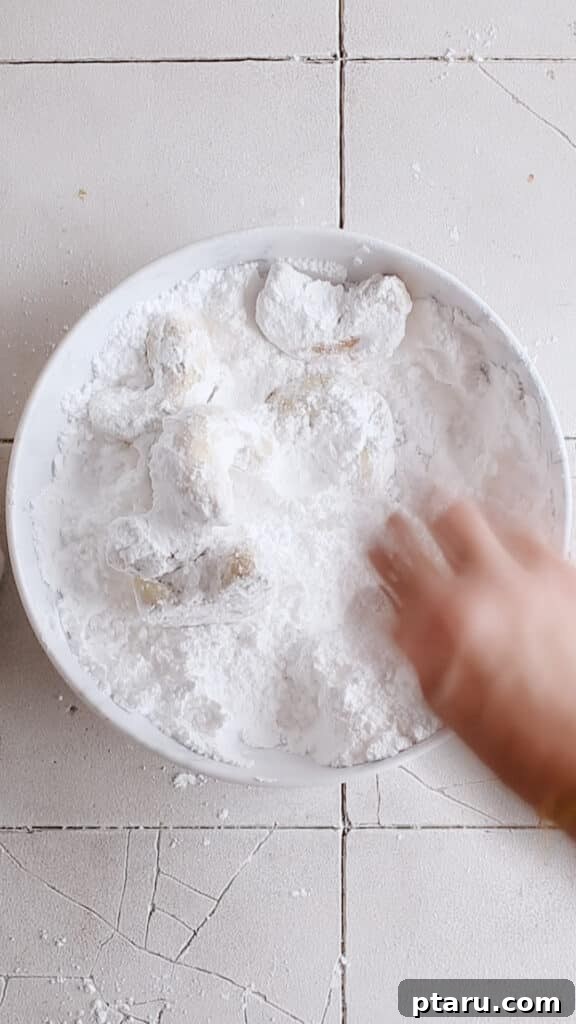 Kourabiedes Traditional Greek Christmas Butter Cookies 10 The process of fully coating Kourabiedes in a generous layer of powdered sugar, ensuring every surface is delightfully covered for that iconic 'snow-kissed' look, making them irresistible.