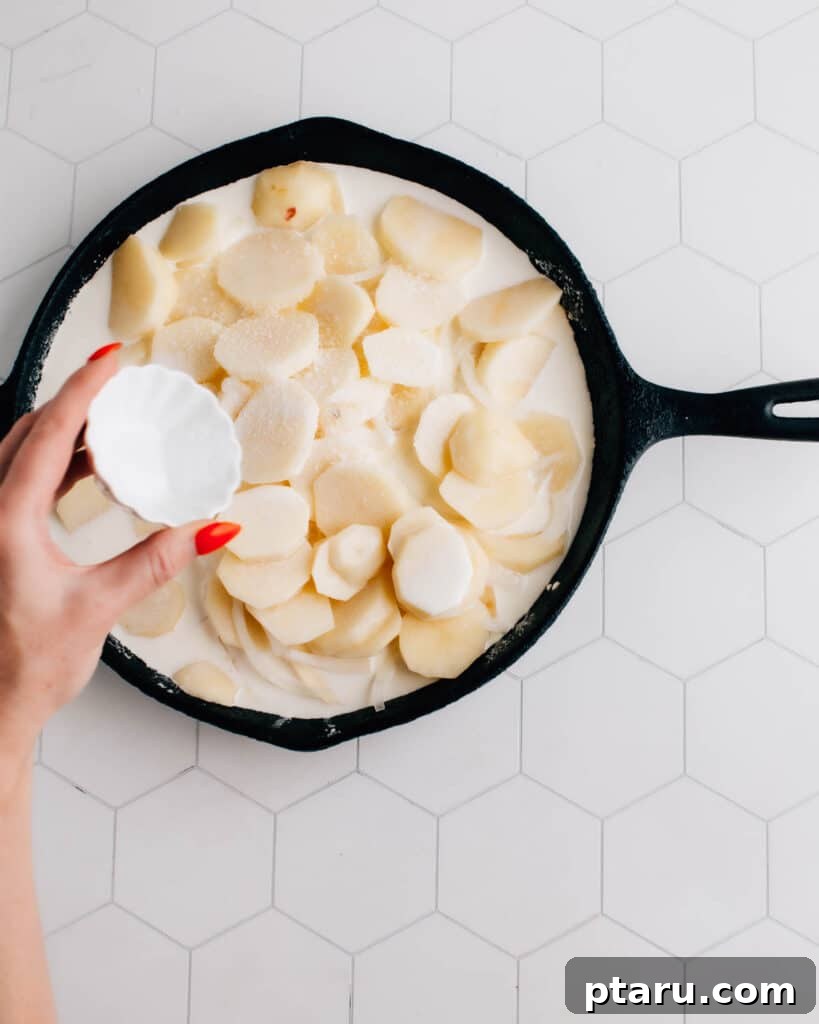 Creamy Gluten-Free Potato Gratin 4 Layering potato slices with onions and sprinkling salt in a cast iron pan.