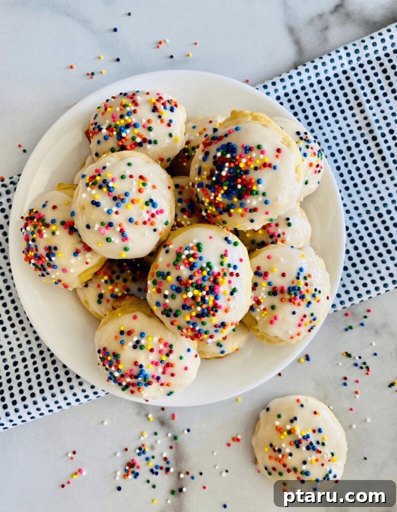 15 Irresistible Italian Desserts to Sweeten Your Christmas 13 A festive stack of soft Italian Ricotta Cookies, each adorned with a sweet frosting glaze and colorful rainbow sprinkles, creating an inviting and traditional Christmas cookie display.