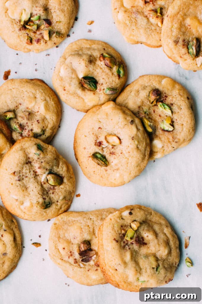 15 Irresistible Italian Desserts to Sweeten Your Christmas 4 A festive pile of lemon pistachio white chocolate cookies, each adorned with green pistachios and white chocolate chunks, presented on parchment paper for an inviting holiday display.