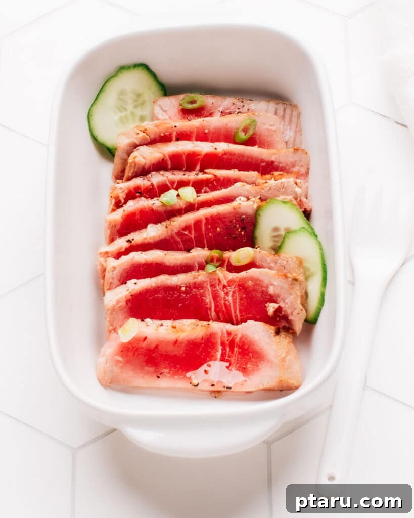Effortless Air Fryer Tuna Steaks 5 Spring onions and cucumber slices top sliced air-fried tuna steak on a rectangular dish.