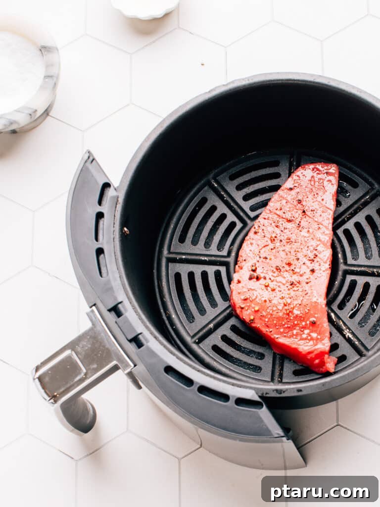 Effortless Air Fryer Tuna Steaks 6 Raw ahi tuna steak in the air fryer basket with salt and pepper.