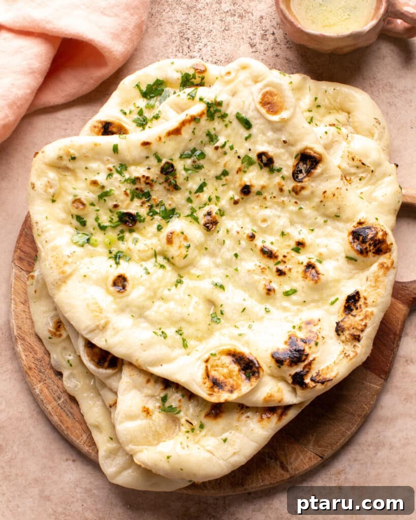Velvety Indian Prawn Korma 5 Freshly baked naan bread, brushed with melted butter and garnished with herbs, on a wooden cutting board.