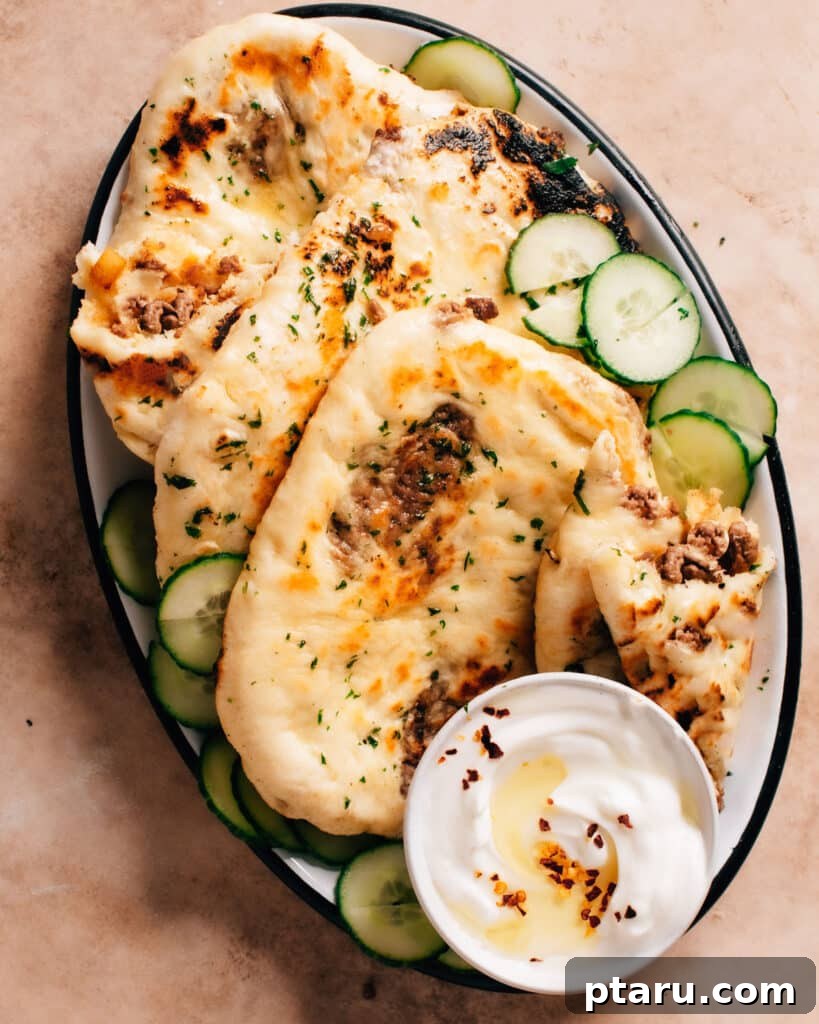Delicious plate of fluffy keema naans served with thin slices of cucumber and a creamy dip, highlighting the golden exterior and the savory meat filling.
