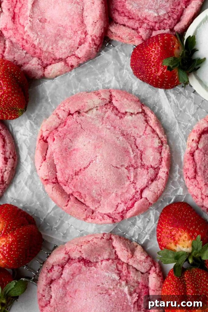 Love at First Bite: Simple Valentine's Sugar Cookies 3 Vibrant pink strawberry sugar cookies, beautifully arranged and surrounded by fresh strawberries, on a rustic surface.