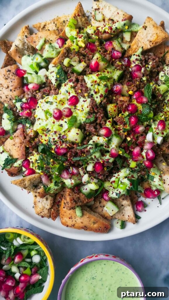 Epic Game Day Nachos: 15 Simple Recipes for Your Crowd 14 Sticky beef fatteh, a Middle Eastern style nacho dish, served on a white ceramic plate with colorful salsa and dip on the side.