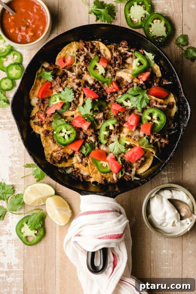 Epic Game Day Nachos: 15 Simple Recipes for Your Crowd 4 Ground Beef Nachos in a sizzling cast iron skillet, garnished with fresh herbs and served with a side of creamy dip.