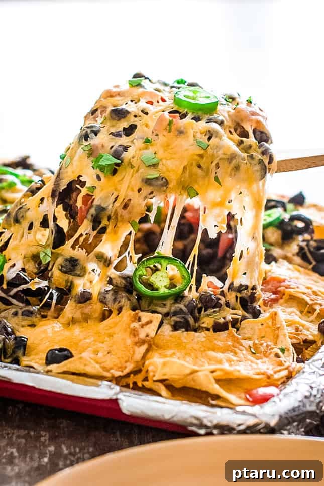 Epic Game Day Nachos: 15 Simple Recipes for Your Crowd 6 A person scooping a generous serving of two-bean vegetarian nachos from a large sheet pan, highlighting the rich toppings.