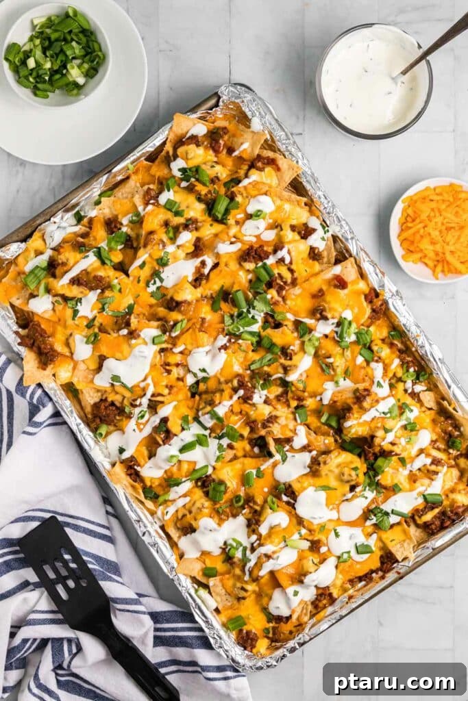 Epic Game Day Nachos: 15 Simple Recipes for Your Crowd 9 A top-down view of loaded chili nachos spread out on a sheet pan, rich with melted cheese and fresh toppings.
