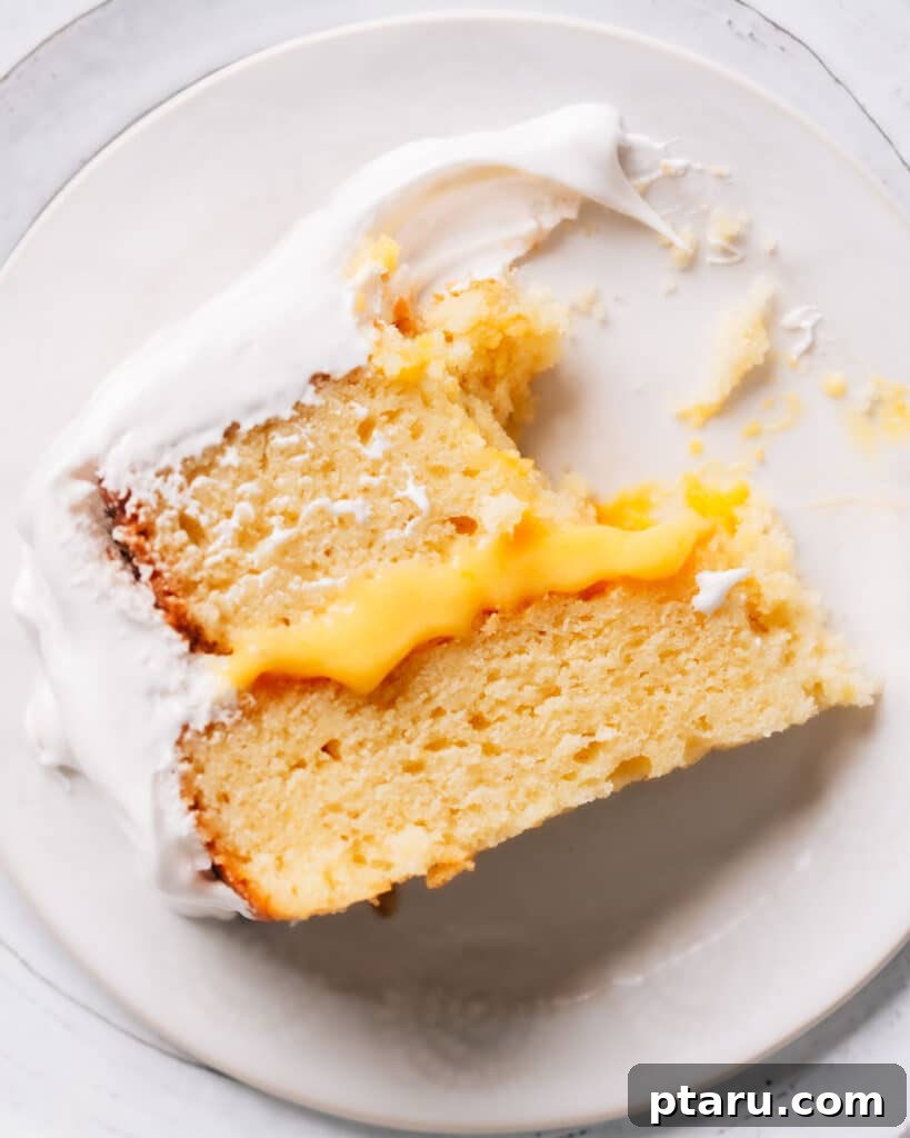 Zesty Lemon Dream Cake 4 A perfect slice of Lemon Curd Cake rests on a white plate, showcasing distinct layers of soft lemon cake, vibrant tangy lemon curd filling, and a fluffy white frosting. A fork has just cut into a portion, ready to be savored.
