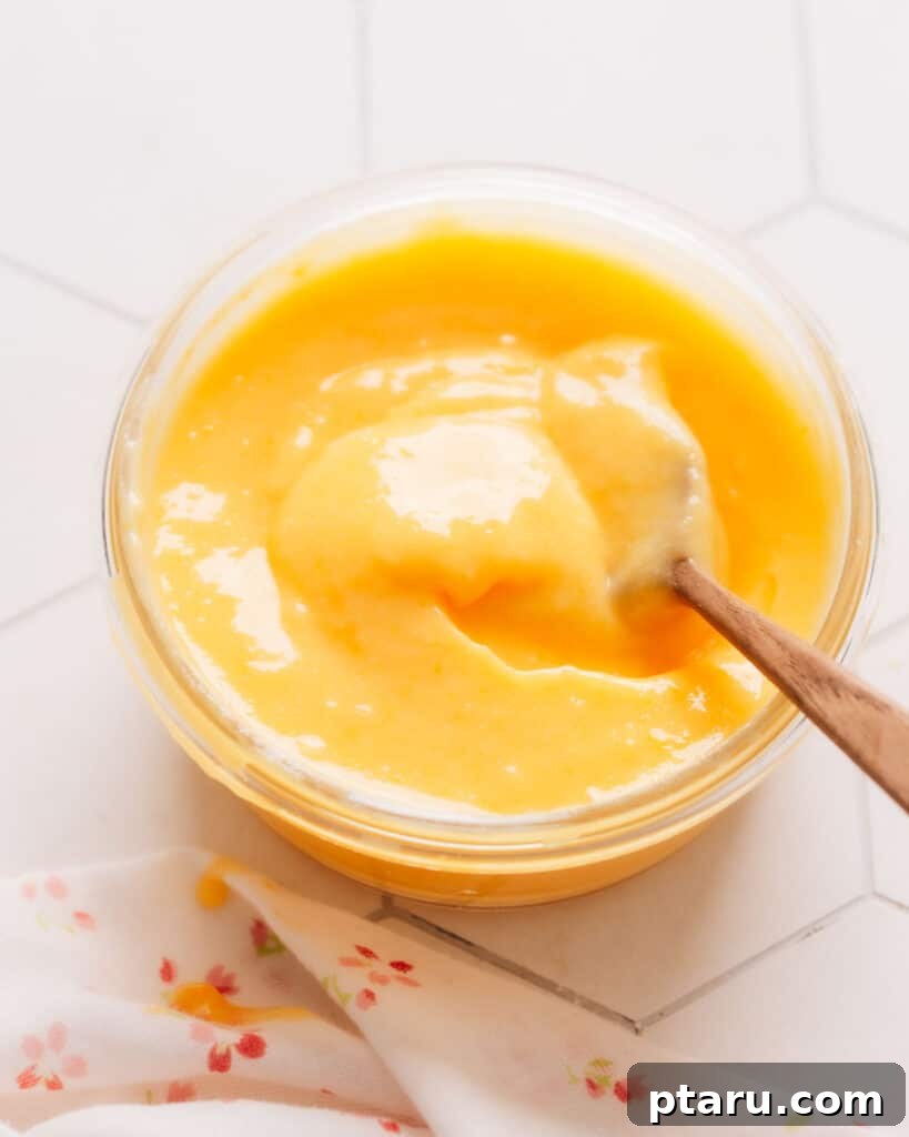 Zesty Lemon Dream Cake 6 A small cup filled with vibrant, fresh lemon curd, with a small wooden spoon resting inside, ready for tasting.