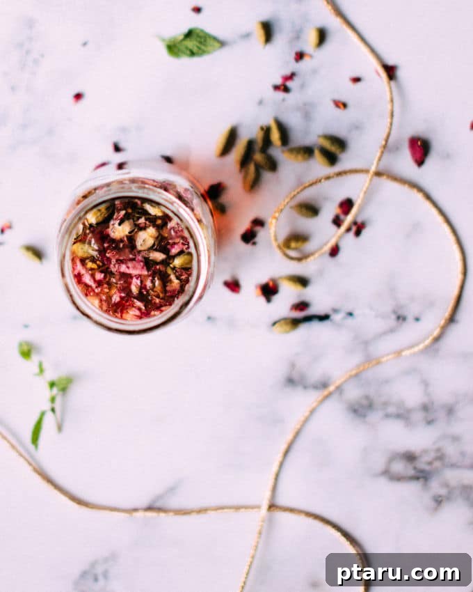 Petal and Spice Elixir 3 Close-up of a hand holding a glass of iced tea, garnished with fresh mint and rose petals, showing the rich color of the Rose and Cardamom Cocktail.