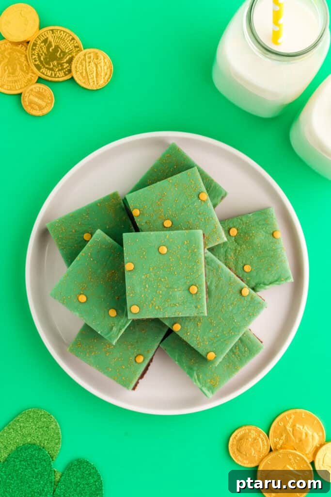 Get Lucky with These Green St. Patrick's Day Desserts 16 A stack of rich chocolate mint fudge squares arranged on a pristine white plate, accompanied by shiny chocolate gold coins, creating a decadent and festive display perfect for St. Patrick's Day.