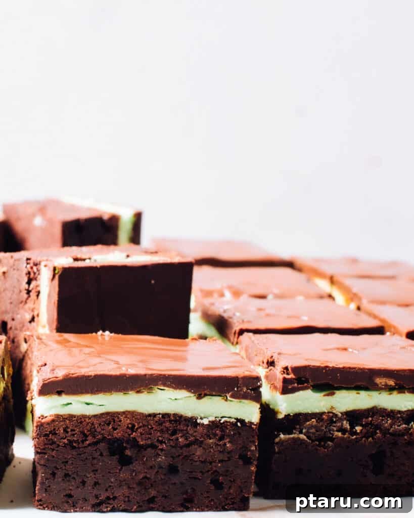 Get Lucky with These Green St. Patrick's Day Desserts 3 A close-up side view of perfectly cut square mint chocolate brownies, showcasing distinct layers of fudgy chocolate, a vibrant green mint frosting, and a thin, dark chocolate top, ready to be enjoyed.