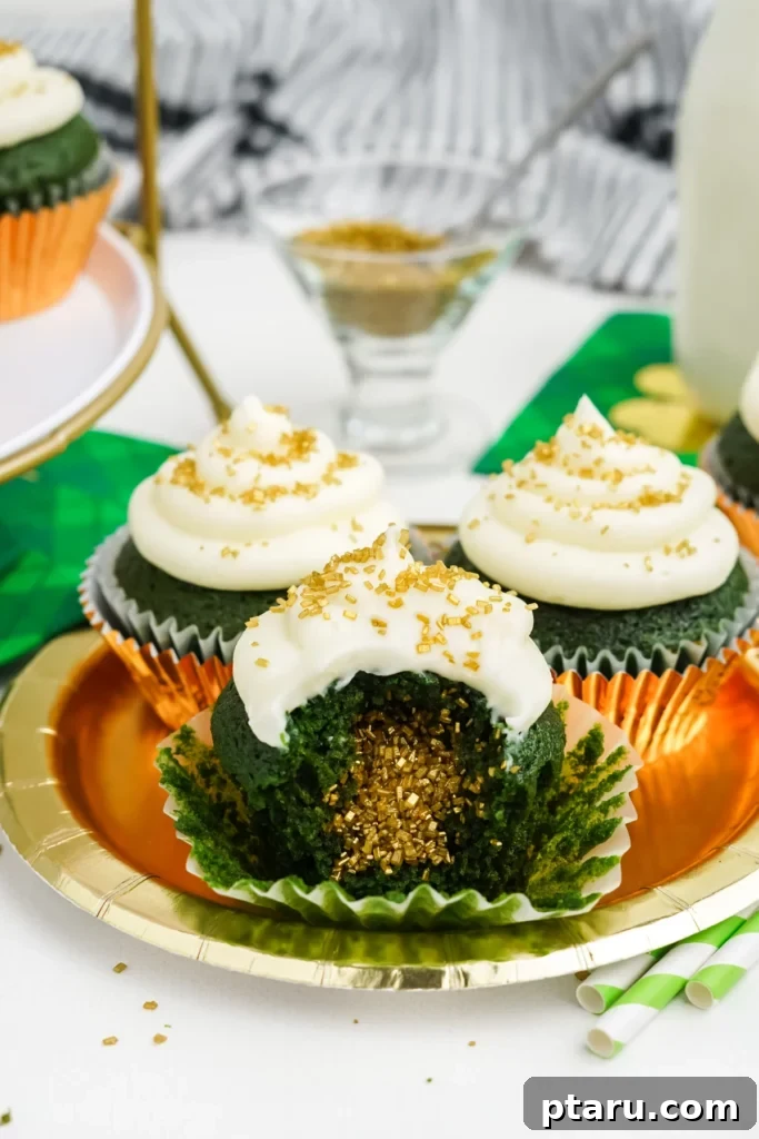 Get Lucky with These Green St. Patrick's Day Desserts 5 Three meticulously arranged green velvet cupcakes, each adorned with a generous swirl of white cream cheese frosting, sit on a golden decorative plate. One cupcake is artfully sliced open, revealing its moist, emerald-green interior sparkling with gold sprinkles, embodying a 'pot of gold' theme.