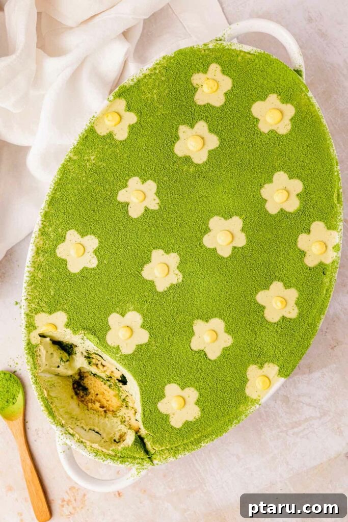Get Lucky with These Green St. Patrick's Day Desserts 7 A generous serving of Matcha Tiramisu presented in a rustic, round bowl, adorned with delicate flower designs dusted with matcha powder. The creamy, vibrant green layers of the dessert are visible, hinting at its rich flavor and smooth texture.