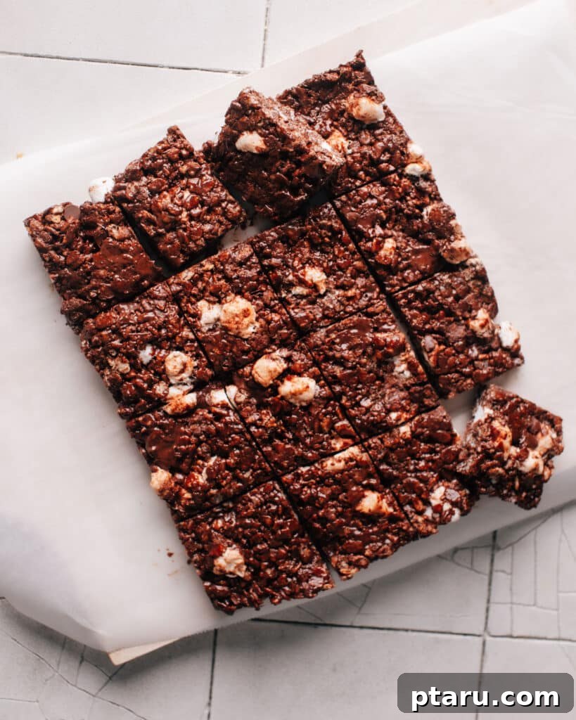 Decadent Chocolate Crunch Bars 9 Chocolate rice krispie treats are cut into even squares on a white parchment paper, ready to be served. The treats have a gooey texture from the melted marshmallows and chocolate chips.