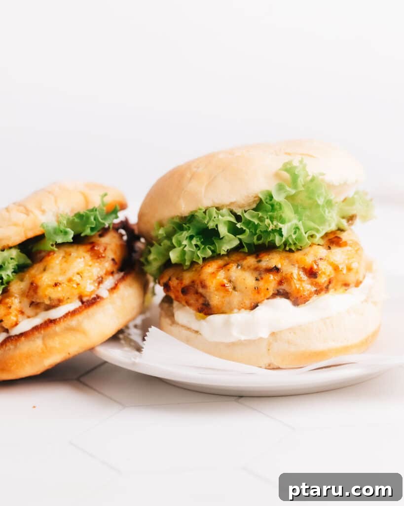 Best Air Fryer Turkey Burgers 2 Two ground turkey burgers on a white plate. The burgers are layered with air-fried turkey patties, lettuce, mayo, and burger buns.