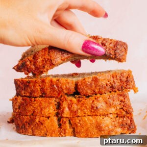 A slice of moist banana zucchini bread being lifted from a freshly baked loaf, showing its soft interior.
