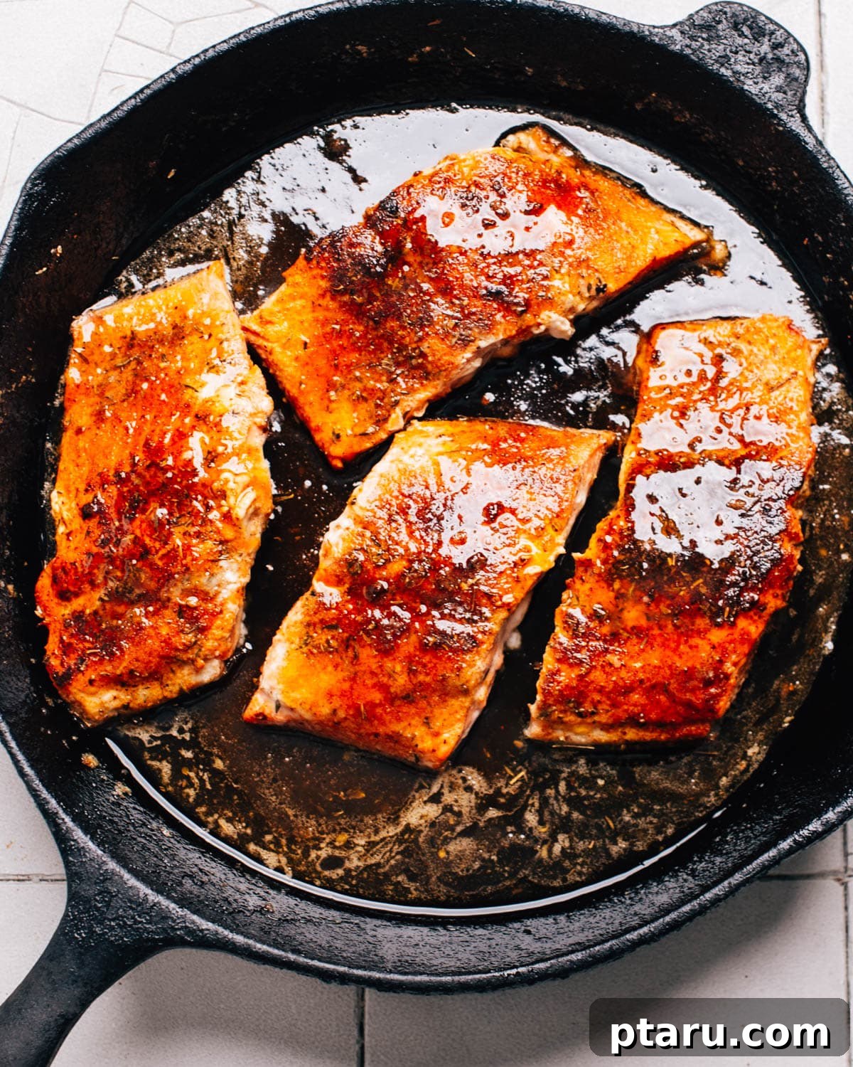 Honey-Butter Glazed Cajun Salmon 2 A cast iron skillet contains 4 salmon fillets that have been seasoned with Cajun spices and brushed with honey butter.