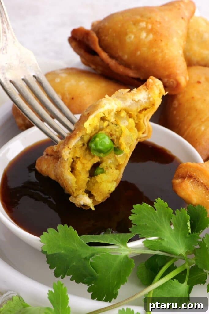 Savory Spiced Potato Samosas 7 A perfectly fried potato samosa with a bite taken, dipped into a vibrant green chutney and held by a fork.