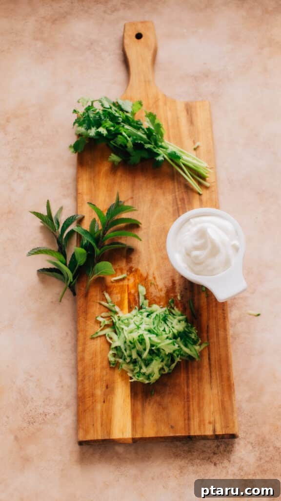 Zesty Indian Cucumber Yogurt Salad 3 Fresh and vibrant ingredients for Indian Yogurt Cucumber Salad laid out on a wooden surface, including creamy yogurt, crisp cucumbers, ripe tomatoes, pungent red onions, garlic cloves, and fragrant fresh herbs like mint and cilantro.