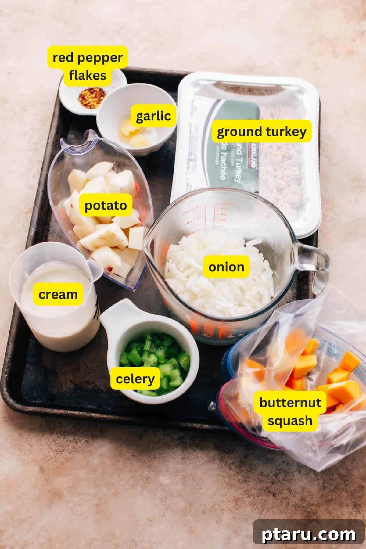 Wholesome Turkey Mince Soup 3 Ingredients for ground turkey soup are laid out on a kitchen countertop including fresh celery, ground turkey, a yellow onion, minced garlic, red pepper flakes, russet potato, butternut squash, and heavy cream. These are the core components for a rich and hearty soup.