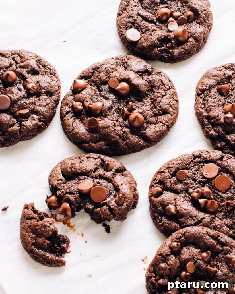 Decadent Mint Chocolate Fudge Cookies 3 Freshly baked Mint Chocolate Cookies with extra chocolate chips on a sheet of parchment paper, cooling down.