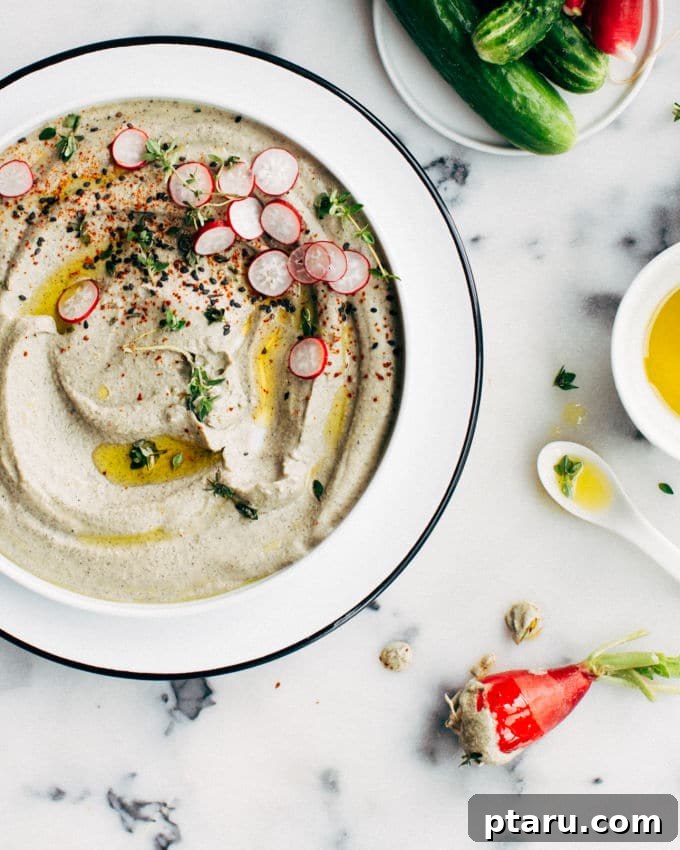 Silky Simit Delights 9 Hummus is presented in a bowl, garnished with sliced radish and sesame seeds.