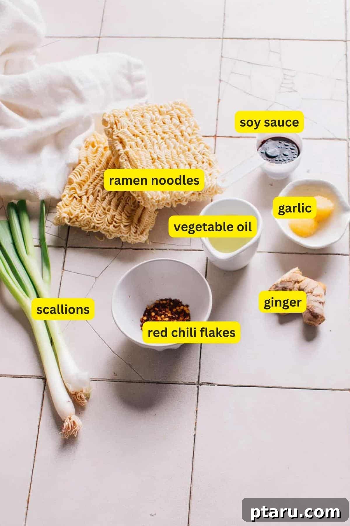 Fiery Chili Oil Ramen 3 Arrangement of fresh ingredients for Chili Oil Ramen on a modern kitchen countertop, including packages of ramen noodles, vibrant green scallions, a bowl of crushed red chili flakes, fresh ginger root, a bottle of vegetable oil, cloves of garlic, and a bottle of soy sauce.
