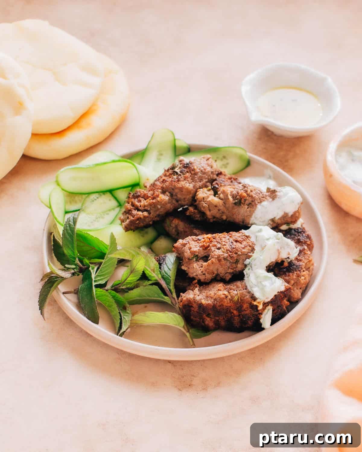 Perfectly Succulent Beef Kafta 2 A plate of beef kafta kabobs with mint and sliced cucumber. Turkish bread is placed behind the plate.