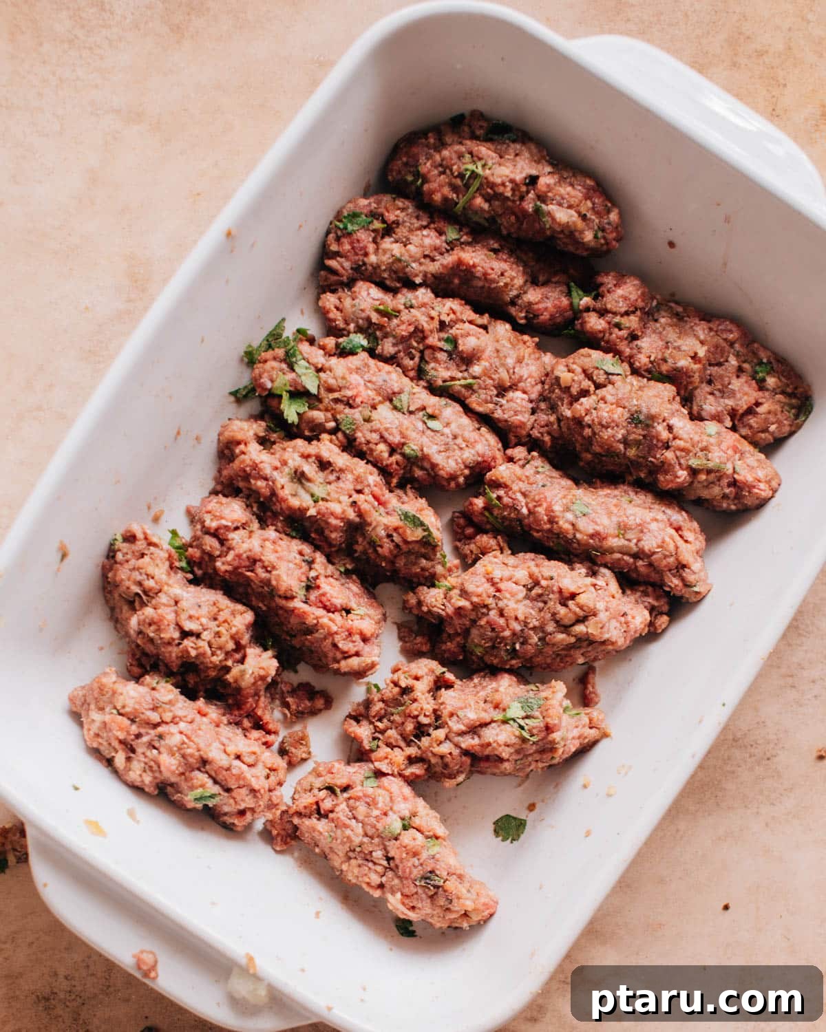 Perfectly Succulent Beef Kafta 7 A white dish with long sausage-like shapes formed from the beef kafta kabob mixture.