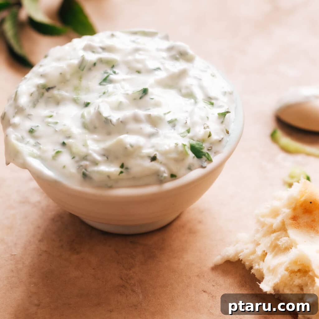 Simple Indian Raita Yogurt Sauce 2 Indian Yogurt Sauce (Raita) in a white bowl, garnished with fresh herbs, against a light background.