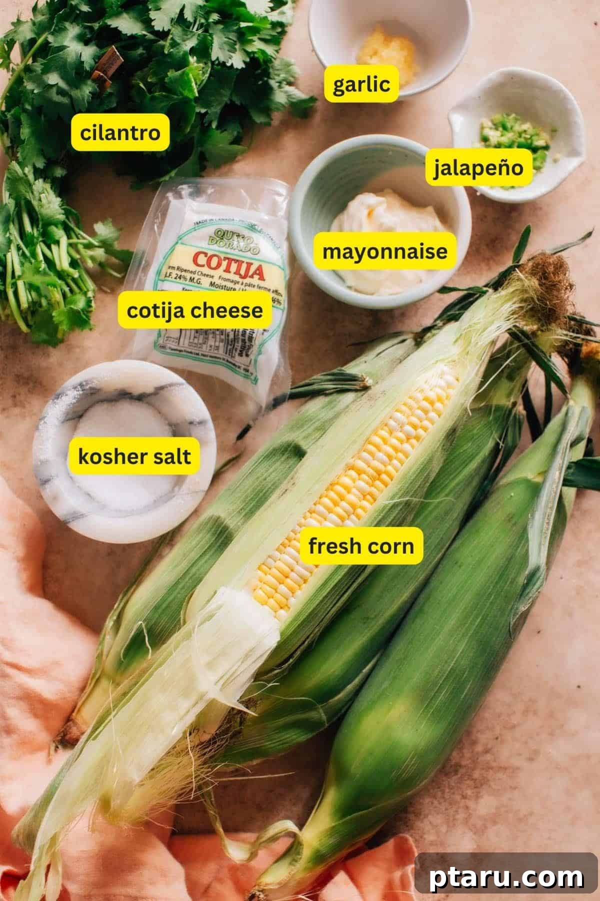 Zesty Mexican Elote Salad 3 A collection of fresh ingredients for a Mexican Roasted Corn Off The Cob recipe, including bright yellow corn cobs, fresh green cilantro, juicy limes, garlic cloves, red jalapeños, and Cotija cheese.