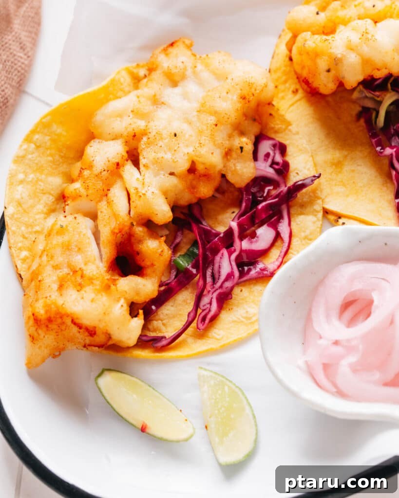 Zesty Fish Taco Slaw 5 Fish tacos with a flavorful cabbage slaw are presented, accompanied by a small cup of sliced onions and lemon wedges for that extra zesty touch.