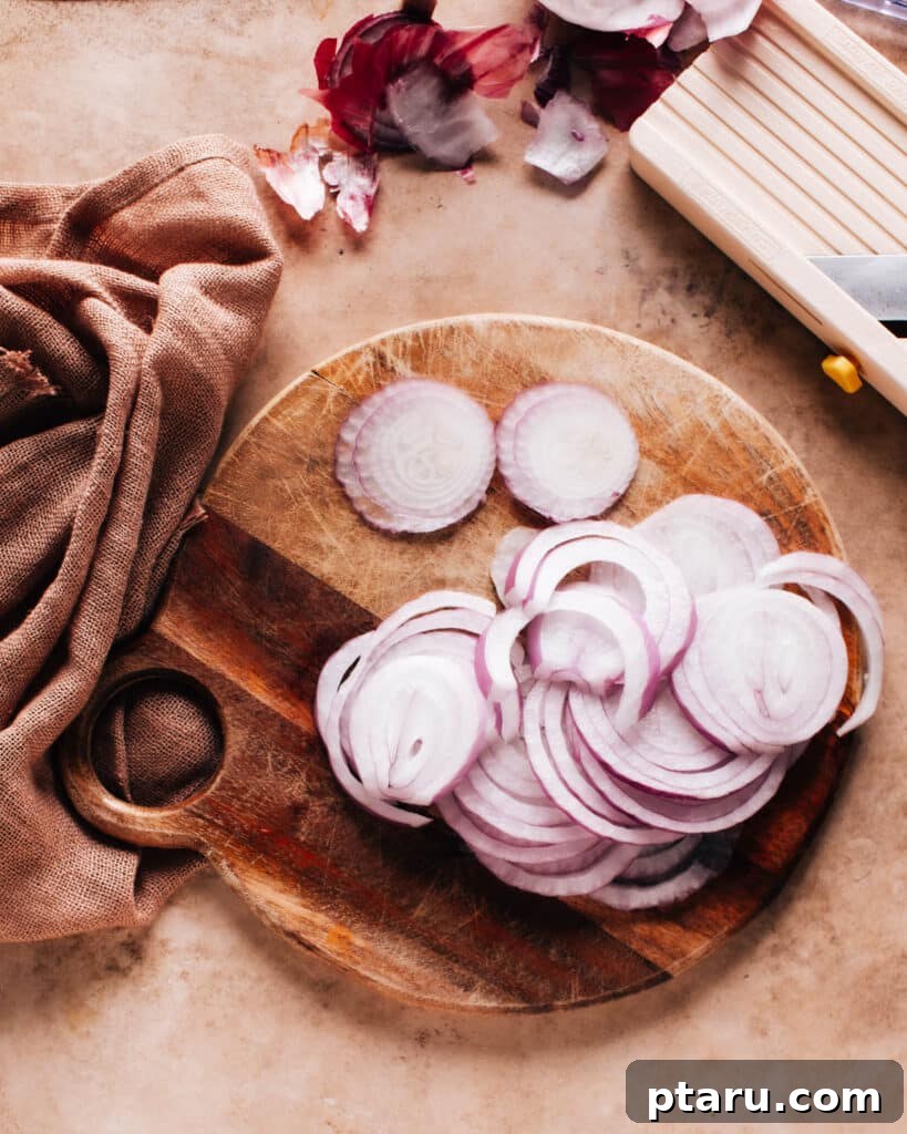 Instant Pickled Onions 6 Thinly sliced red onions on a wooden chopping board with a mandoline slicer nearby, illustrating the importance of thin cuts.