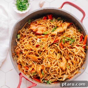 Chicken chow mein noodles in a large skillet, topped with fresh green onions.