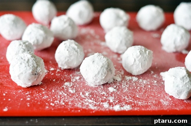 Decadent Chocolate Snow Bites 5 Row of chocolate snowball cookie dough balls generously rolled in icing sugar, neatly arranged on a parchment-lined baking sheet, ready for the oven.