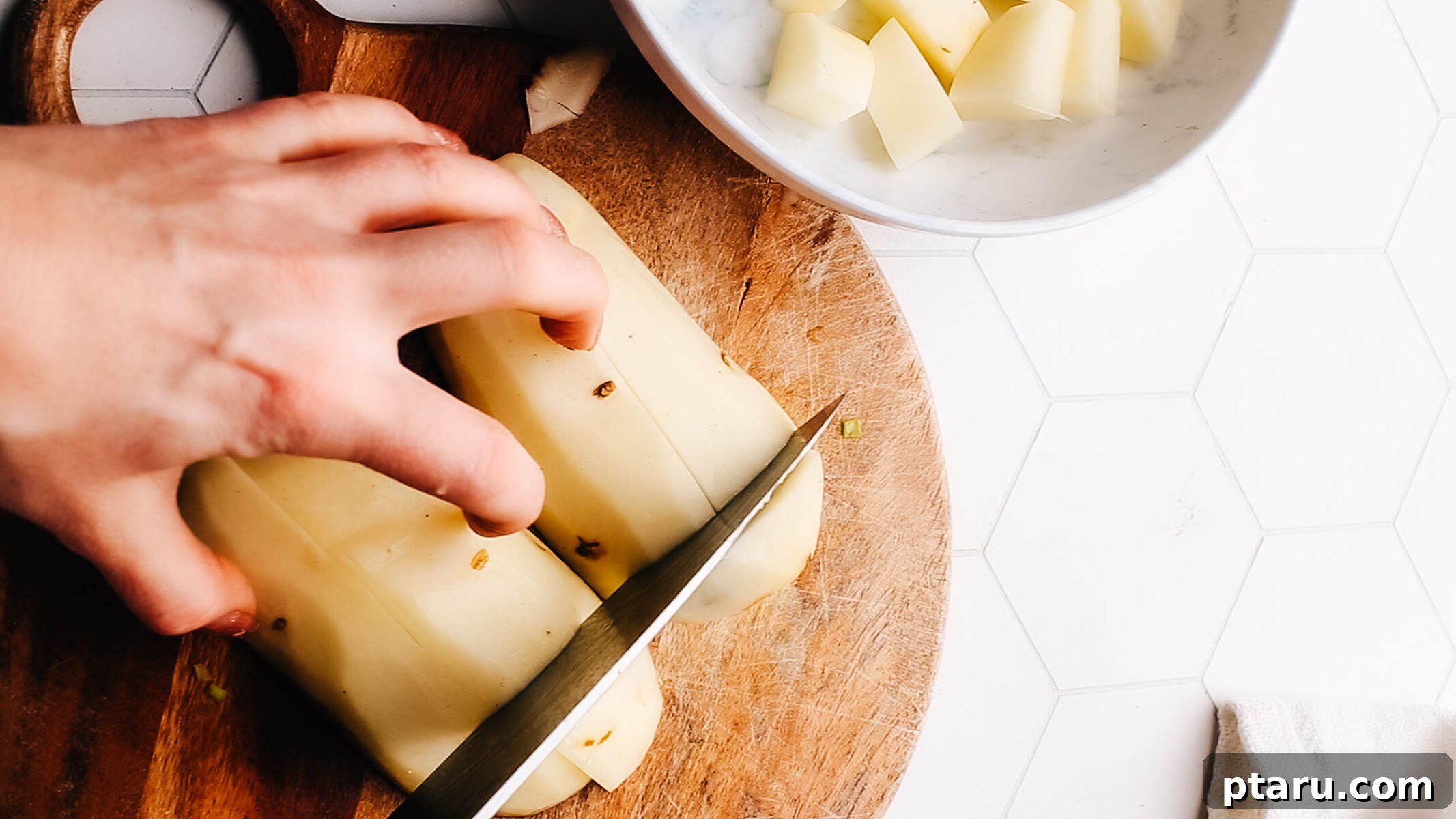 The Only Mashed Potatoes Recipe Youll Ever Need 3 A chef's hands chopping Russet potatoes on a wooden cutting board, preparing them for boiling.