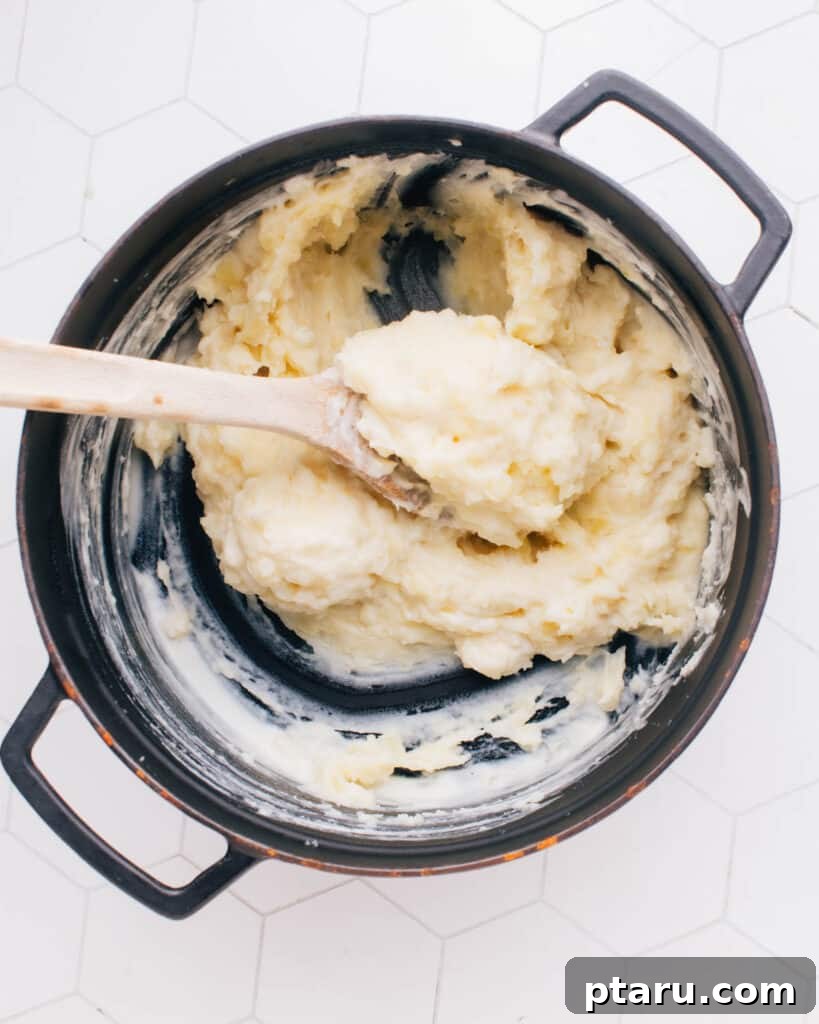 The Only Mashed Potatoes Recipe Youll Ever Need 9 A spatula gently blends the warm cream and butter mixture into a pot of freshly mashed potatoes, creating a smooth and creamy consistency.