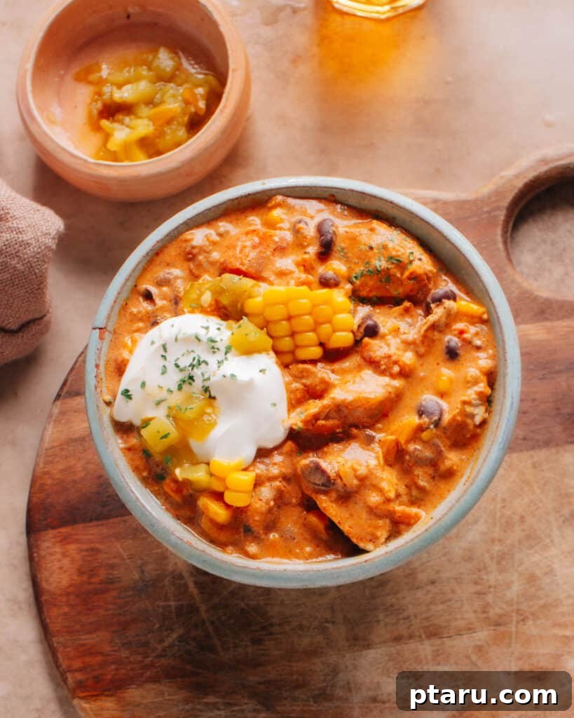 Velvety Cream Cheese Chicken Chili 2 A hearty bowl of Cream Cheese Chicken Chili, generously topped with fresh corn kernels, vibrant green chilies, and a dollop of soft cream cheese, ready to be enjoyed.