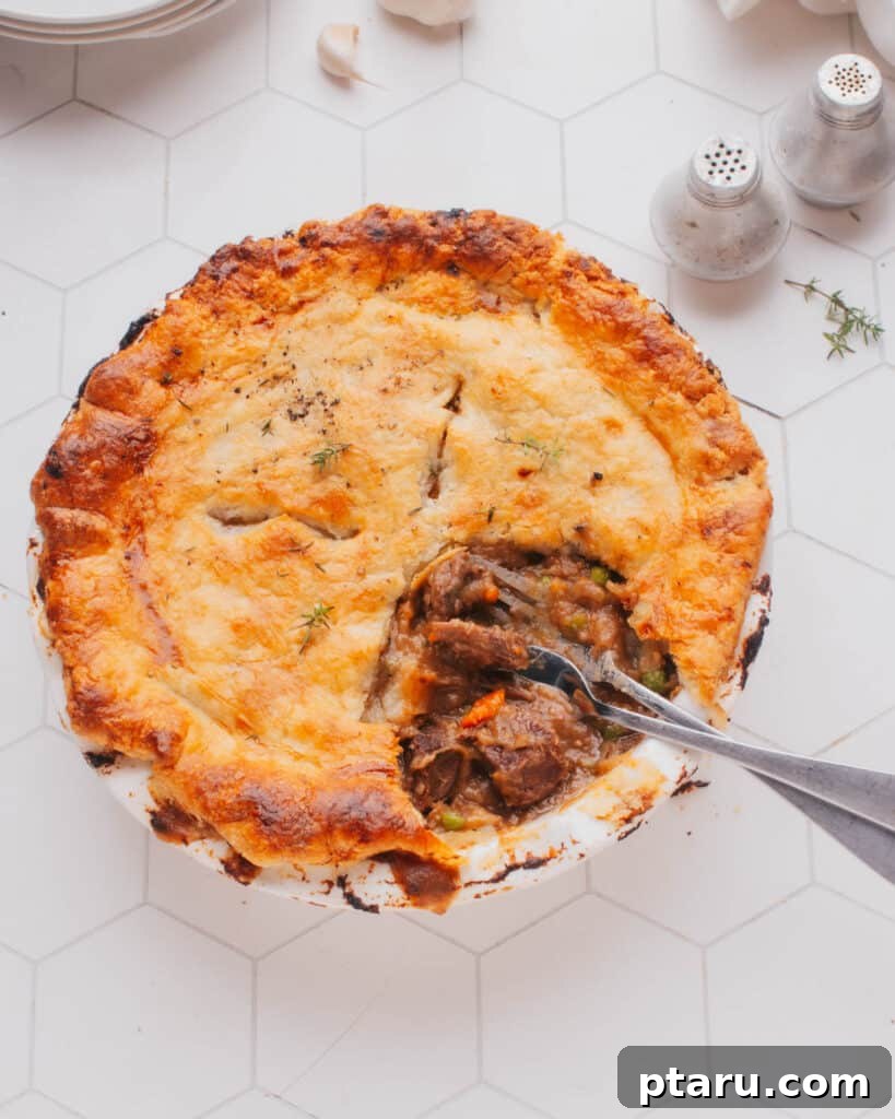 Homestyle Beef & Veggie Pie 2 A delicious Beef Pot Pie with a piece removed, revealing the tender beef and rich gravy inside, accompanied by two forks, ready to be enjoyed.