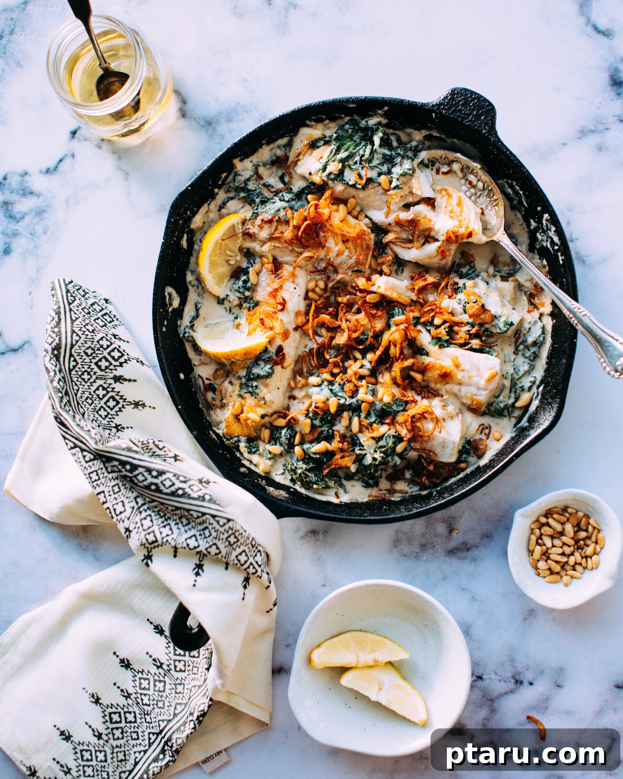 Fish with Tahini Sauce and Kale Close-up of seared white fish with creamy tahini sauce and wilted kale in a skillet, ready to be served.